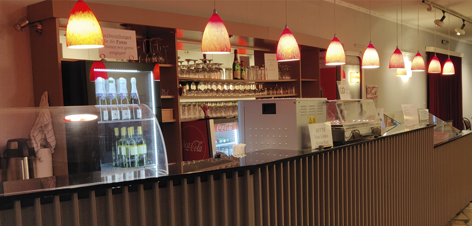 Die Theater-Bar im Foyer mit beleuchteter Theke, Weingläsern und farbigen Hängelampen